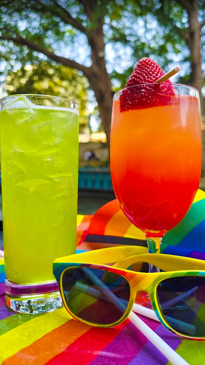 Bright yellow and red cocktails in front of rainbow sunglasses.