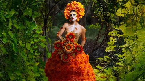 Woman dressed in orange floral dress with sugar skull makeup.