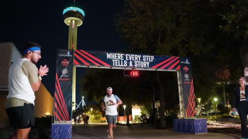 Man crossing finish line in front of Tower of the Americas at San Antonio Marathon.