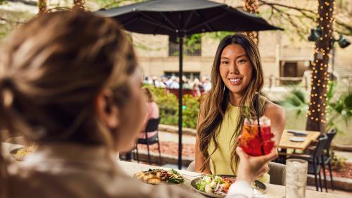 Woman accepting drink from waitress and smiling with San Antonio River Walk behind her.