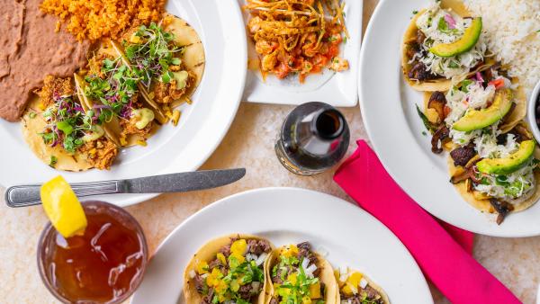 Overhead view of assorted taco plates, pink napkin, bottle, and iced tea at Acenar Restaurant.