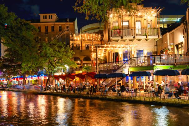 Restaurants along the River Walk in San Antonio at night with lights reflecting off the water.