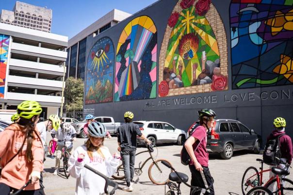 People in bike helmets with their bikes in front of mural in downtown San Antonio.