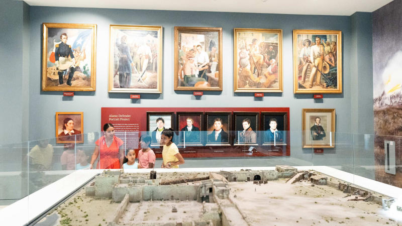 Family viewing exhibit at Ralson Collection Center in San Antonio at the Alamo with historical portraits in background.
