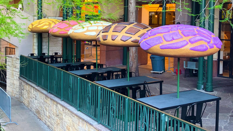 Outdoor restaurant seating with umbrellas in the shape of colorful conchas.