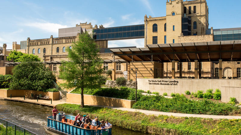 River barge drifting along river in front of San Antonio Museum of Art