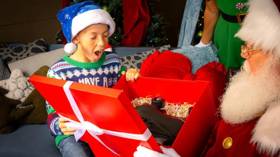 Child with Santa hat on opening present in front of Santa.