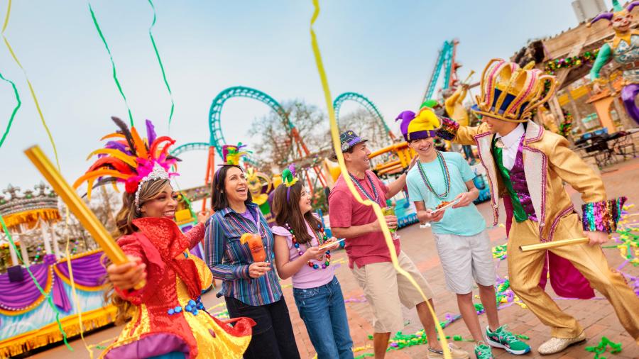 Family laughing with costumed characters at Six Flags Fiesta Texas Mardi Gras event.