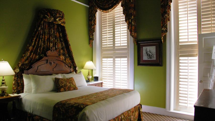 Single-bed hotel room at Historic Menger with green walls and antique lamps.