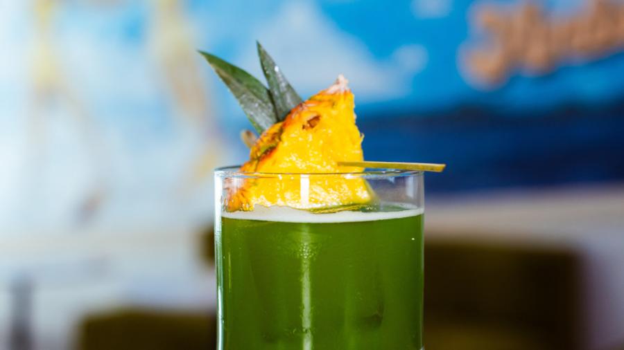 Green cocktail drink with pineapple on top.