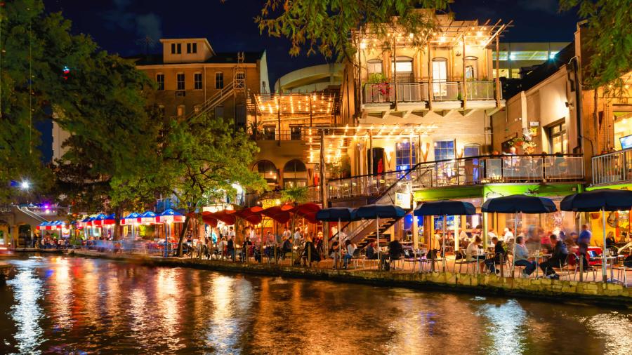 Restaurants along the River Walk in San Antonio at night with lights reflecting off the water.