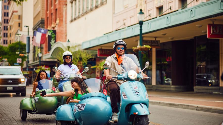 SiDECARS SA Vespa with driver and rider cruising in San Antonio.