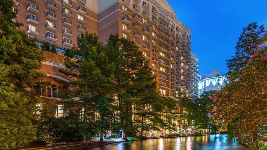 Exterior view of hotel building at night by San Antonio River Walk.