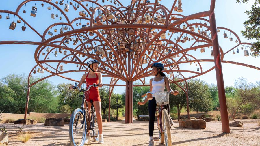 Two girls in front of public art on bikes at Mission Reach in San Antonio.
