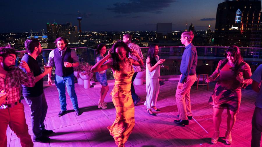 Crowd dancing around woman at rooftop bar in San Antonio.