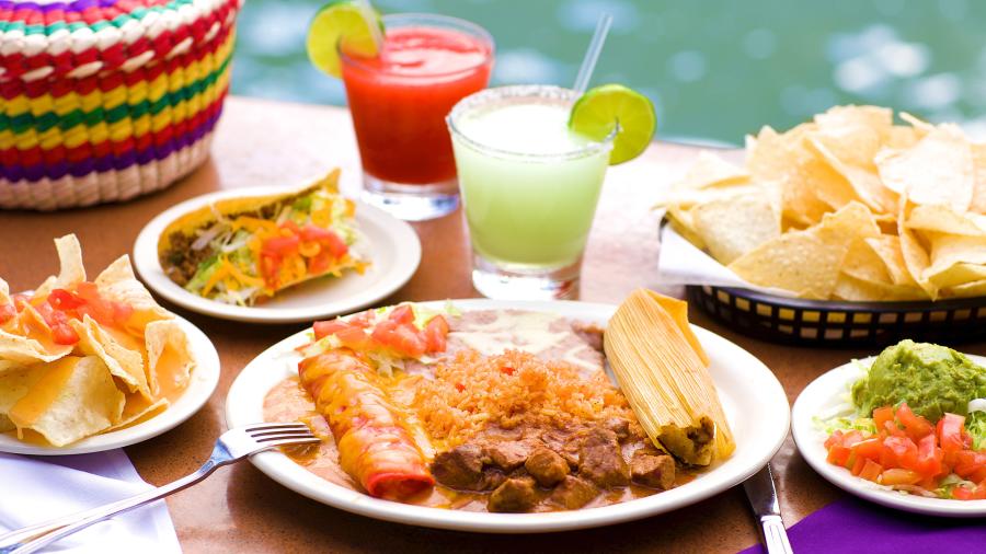 Plate of enchiladas, rice, and beans next to assorted side items and two margaritas at Casa Rio.