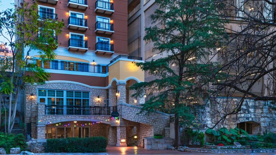 Exterior view of hotel at dusk with lit trees on either side.