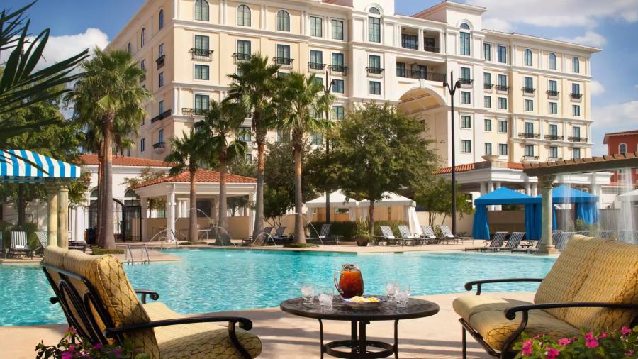 Two hotel pool lounge chairs facing each other with table and iced tea in between them and pool in background.