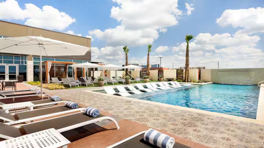 Outdoor hotel pool with lounge chairs and palm trees.