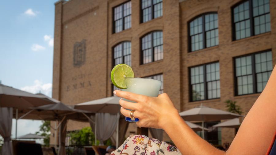 Woman holding glass with cool drink and lime and Hotel Emma in the background.