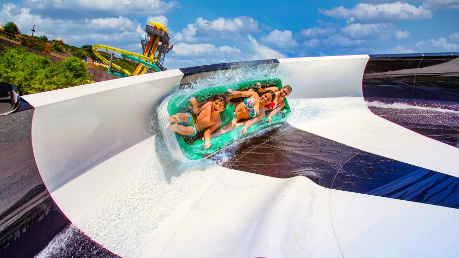Group of three people on black and white water slide at Hurricane Harbor at Six Flags Fiesta Texas.