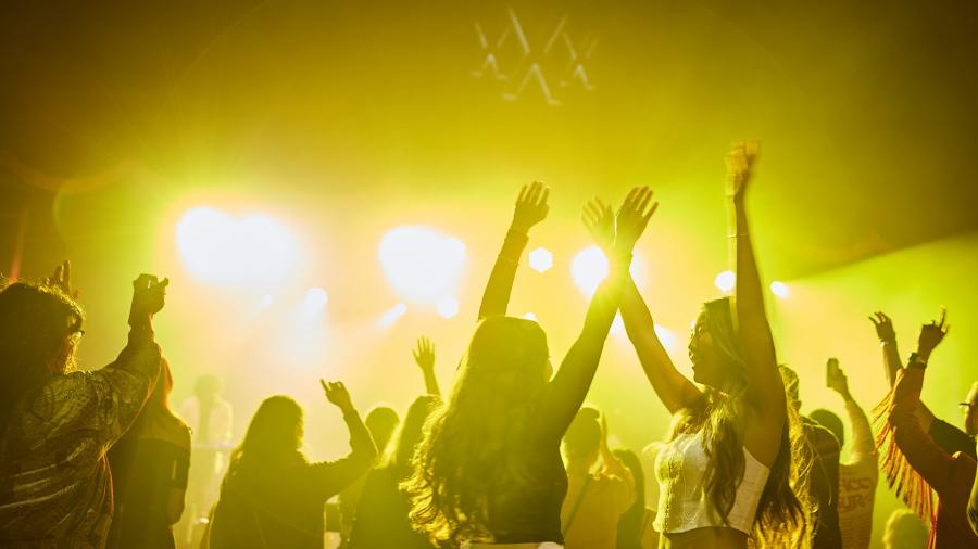 People dancing with their arms in the air in yellow light