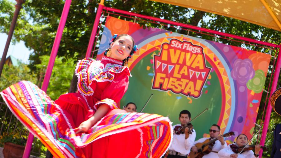 Folklorico dancer in red dress dancing with mariachi band behind her.