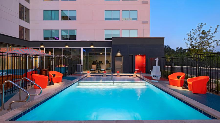 Hotel pool at dusk lit up at night with red orange lounge chairs surrounding it.