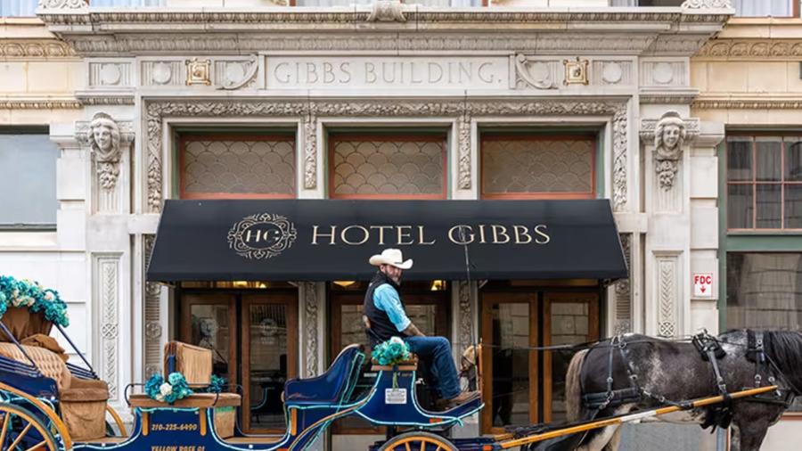 Man on horse and carriage in front of awning with "Hotel Gibbs" in print on it.