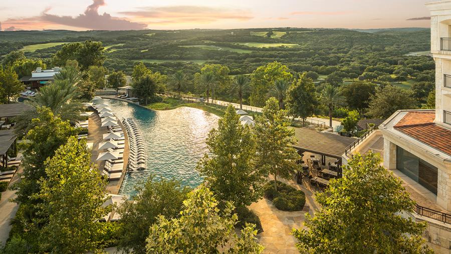 Bird's eye view of resort with pool and sunset in distance.