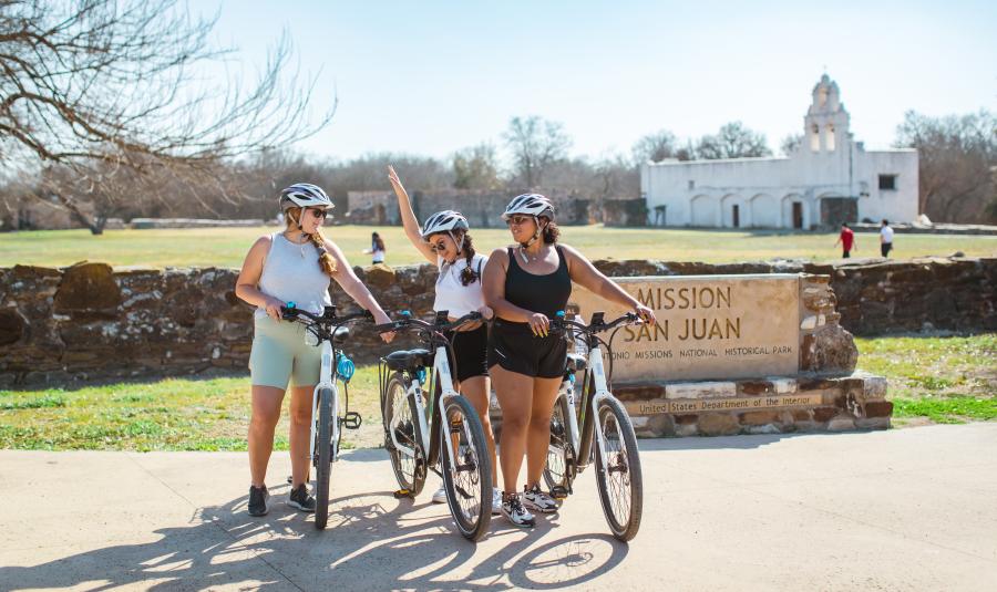 Three girls posing with bikes in front of Mission San Jose in San Antonio.
