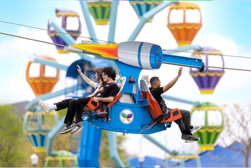 Riders waving with Ferris wheel in background