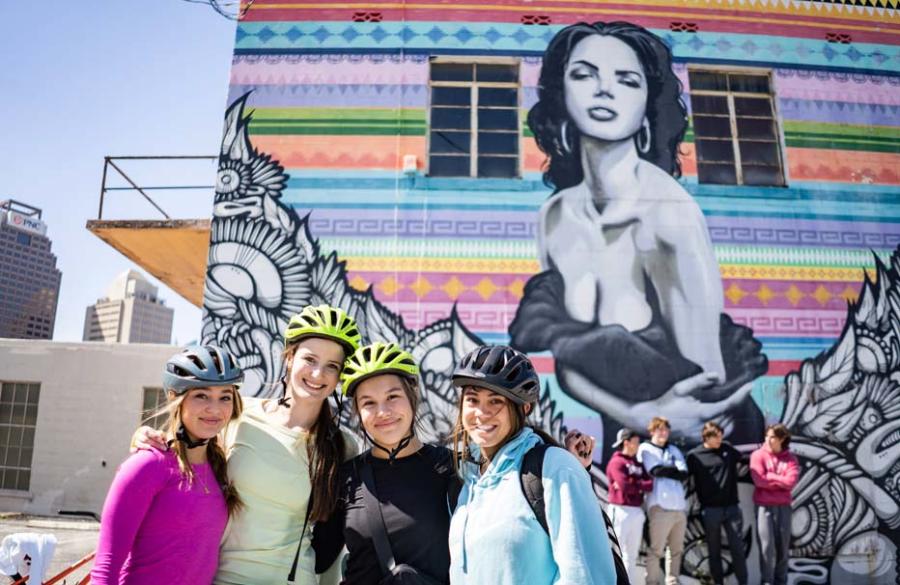 Four girls with bike helmets posing for photo in front of mural of woman in San Antonio.