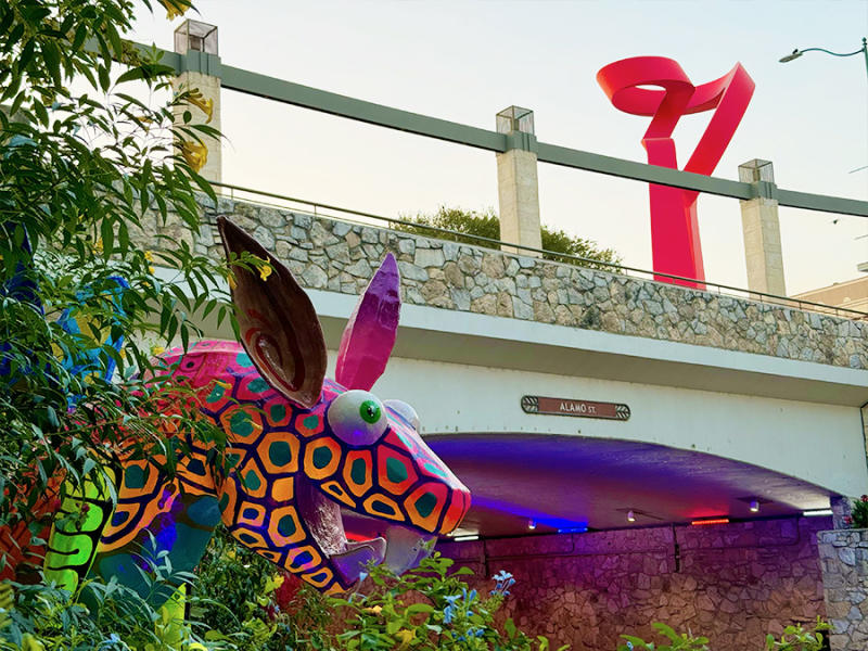 colorful characters with riverwalk bridge lit up under