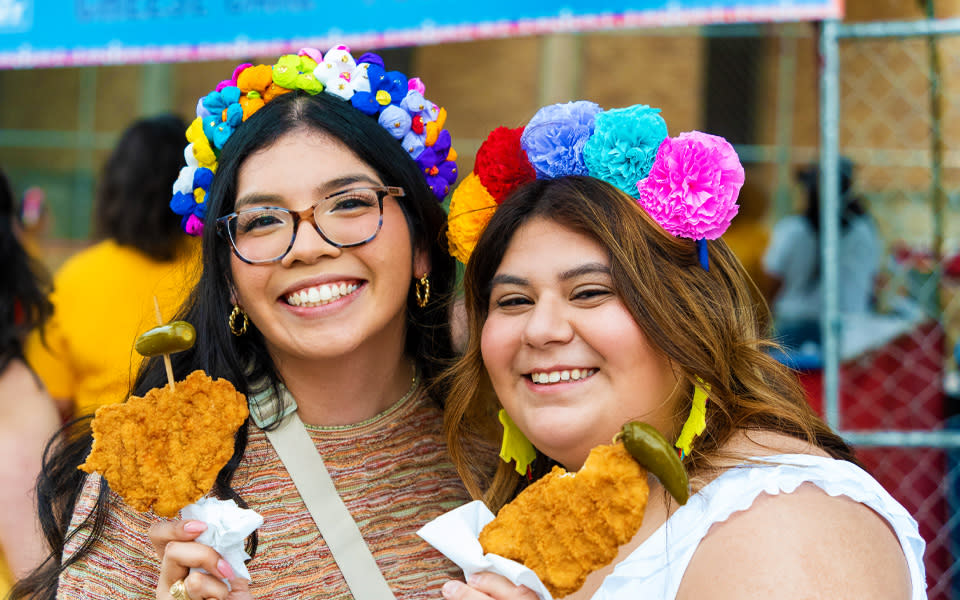 Two girls holding chicken on a stick wearing flower crows at Fiesta San Antonio.