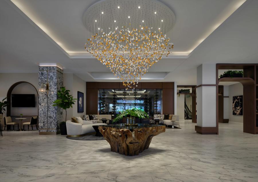 Modern hotel lobby with marble floors and a large chandelier above a wooden table