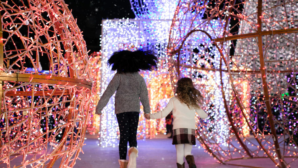 Two girls running toward large holiday light displays.
