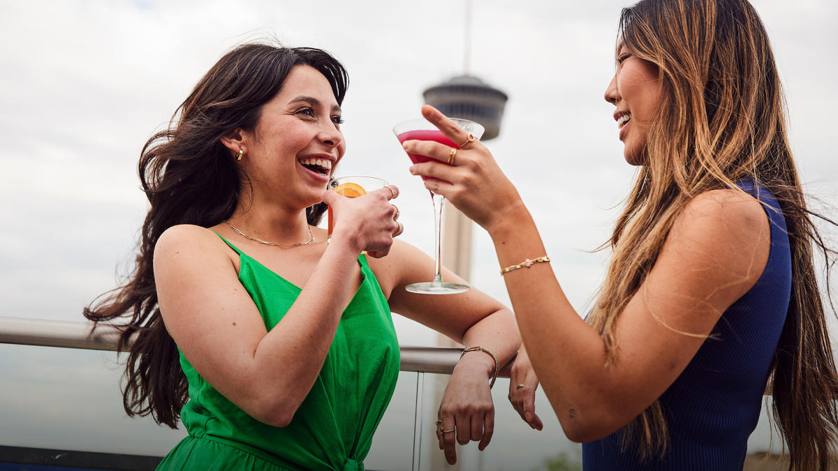 Two girls laughing and enjoying drinks with Tower of the Americas in background