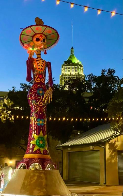 Large catrina statue in La Villita in San Antonio at dusk with a large building in the backround