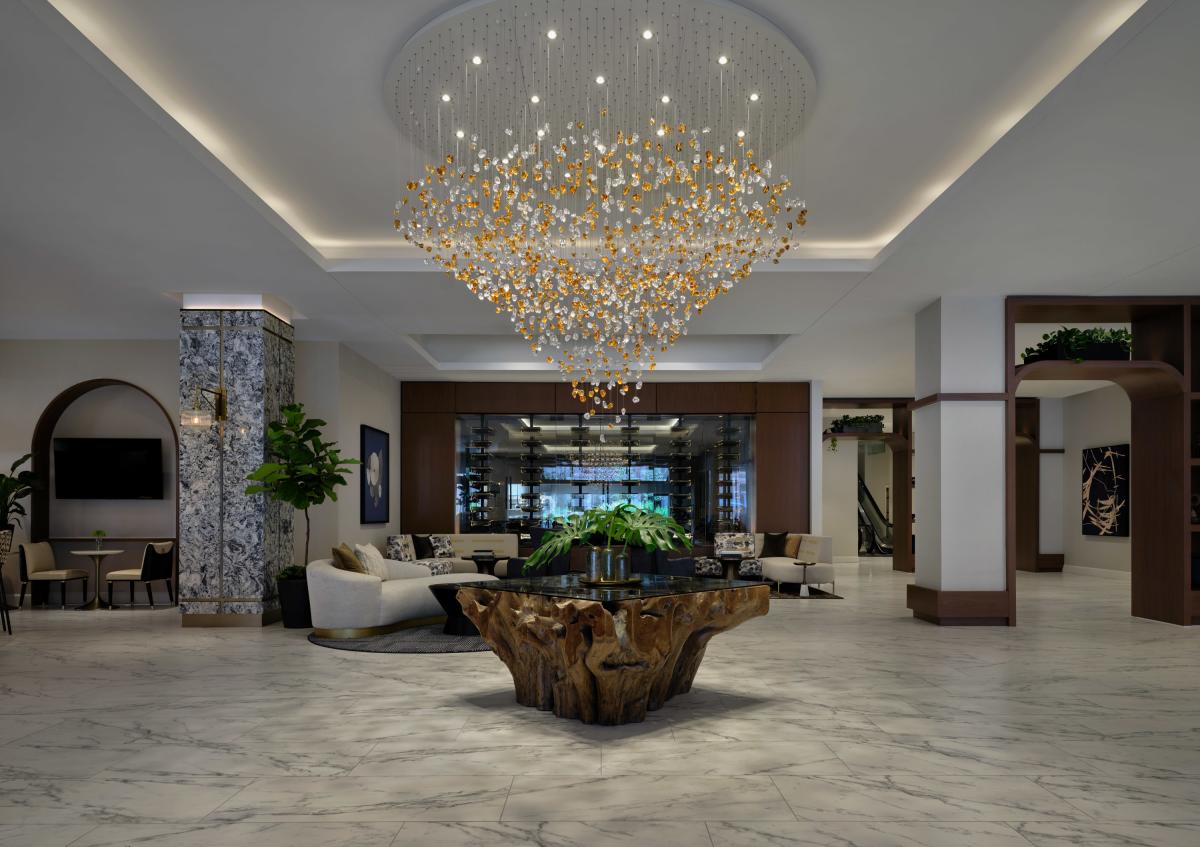 Modern hotel lobby with marble floors and a large chandelier above a wooden table