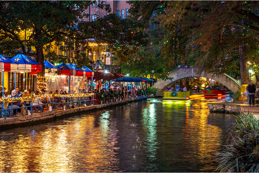 Calm river along River Walk with holiday lights and patio dining in background