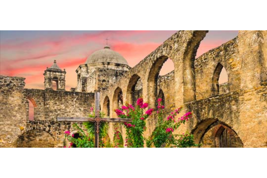 Wooden cross at San Antonio Missions National Historical Park with pink sky in background.