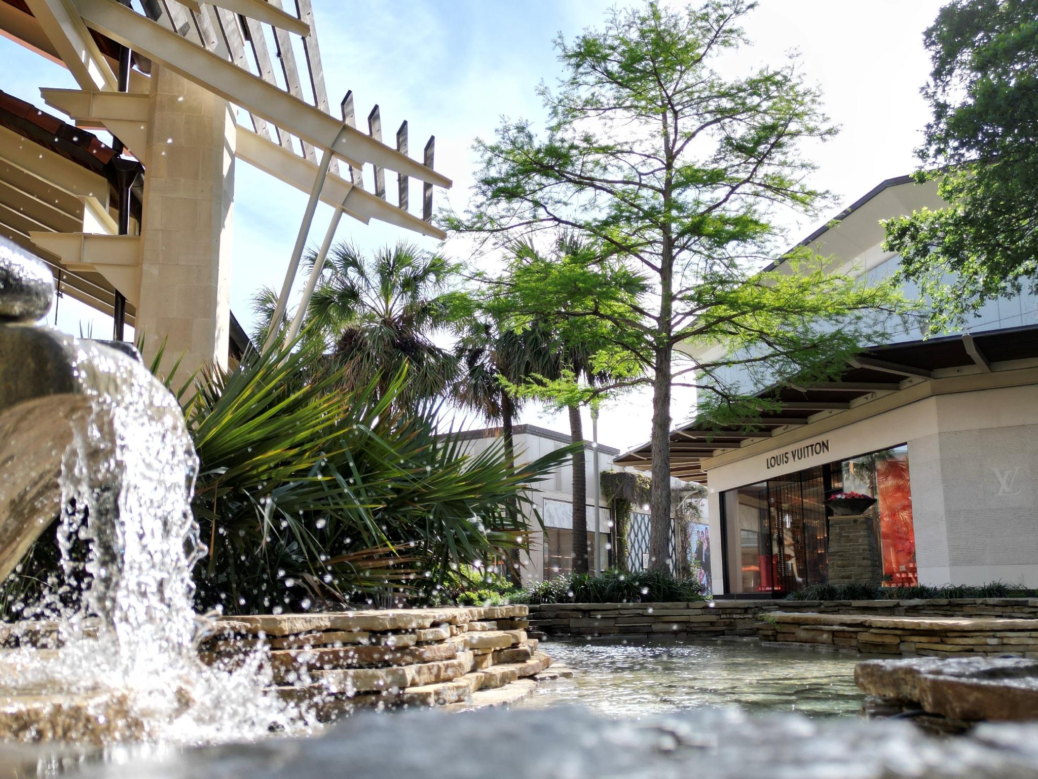 Water fountain and trees in front of storefronts at The Shops at La Cantera.