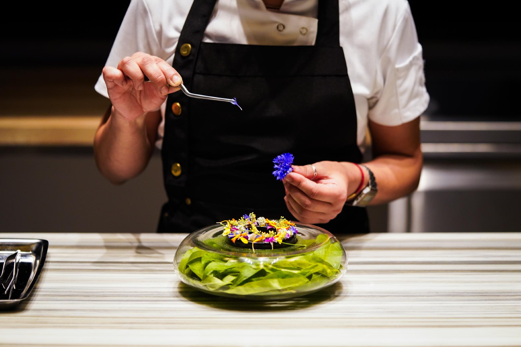 Woman holding flower and tweezers decorating elevated dish at Nicosi.