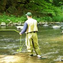 a man stands at the bank of a river casting a fishing line into the water