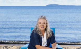 Snapshot of Traverse Tourism employee, Tracy Jenkins, sitting on a blue chair on the shore of Clinch Park beach in Traverse City, Michigan