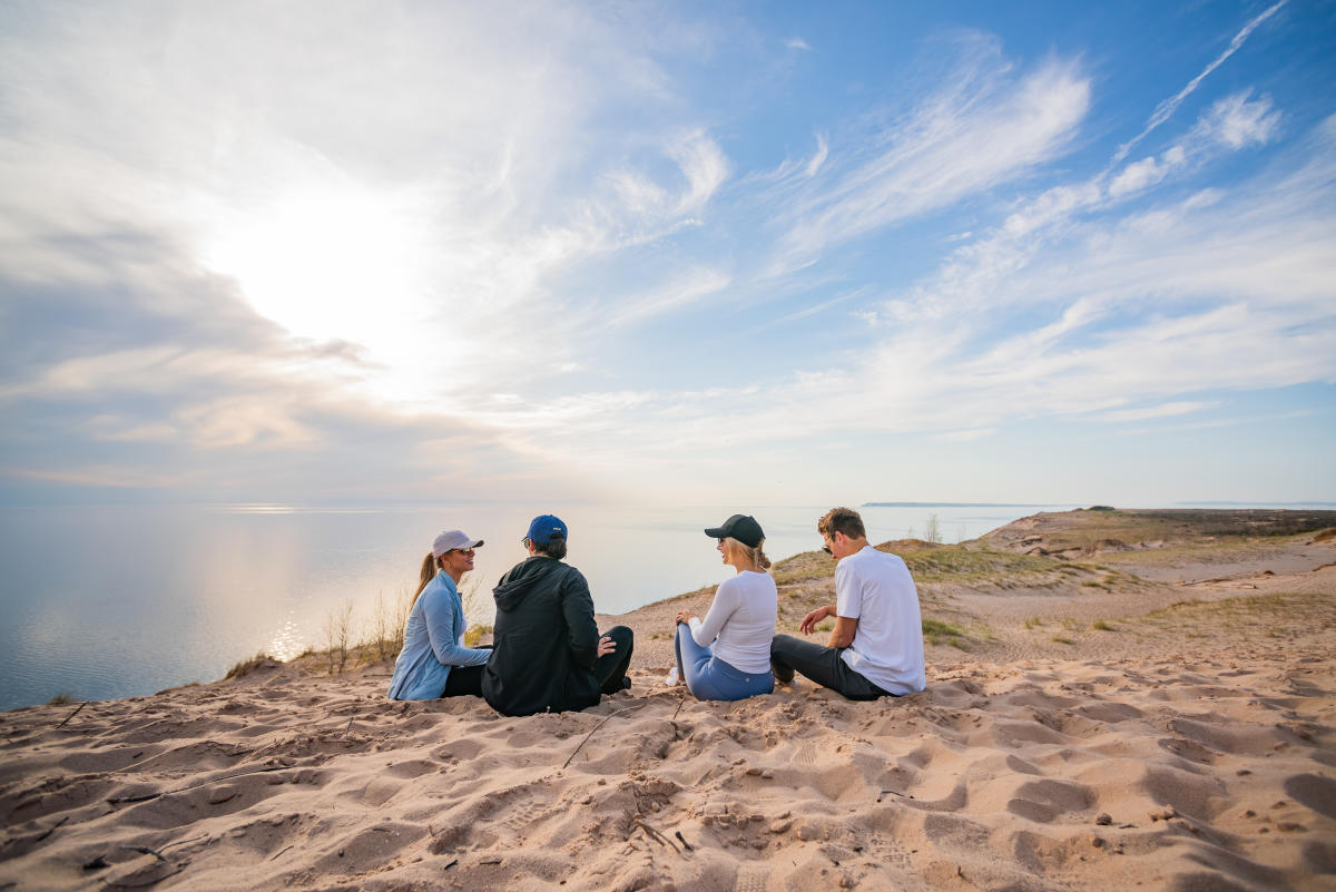 group of friends sitting on the sleeping bear dunes facing Lake Michigan