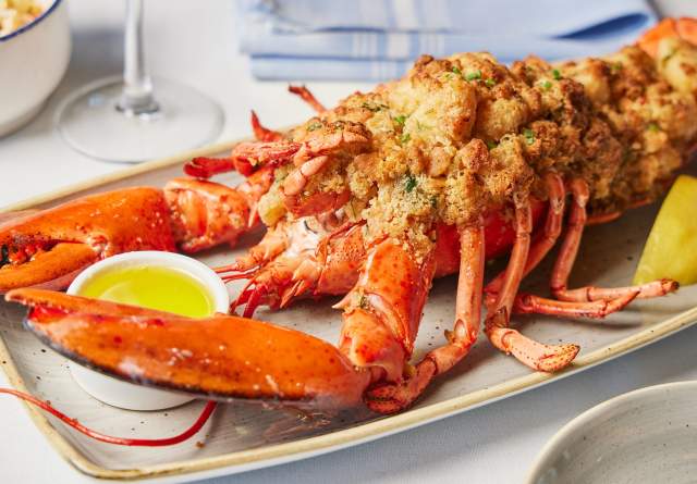 Baked lobster with fried meat and melted butter placed on a plate with a lemon slice
