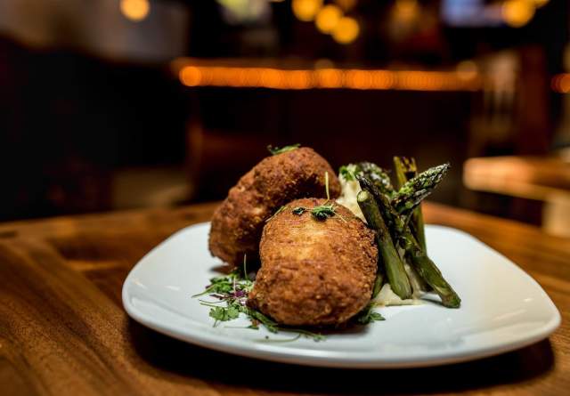 Fried crab cake with garnish and baked asparagus on a white plate, placed on a wooden table at the Spring House Tavern