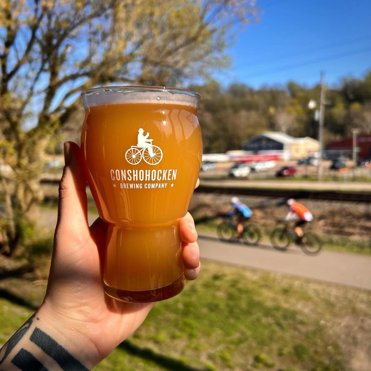 Person holds a pint of beer in front of the Schuylkill River Trail